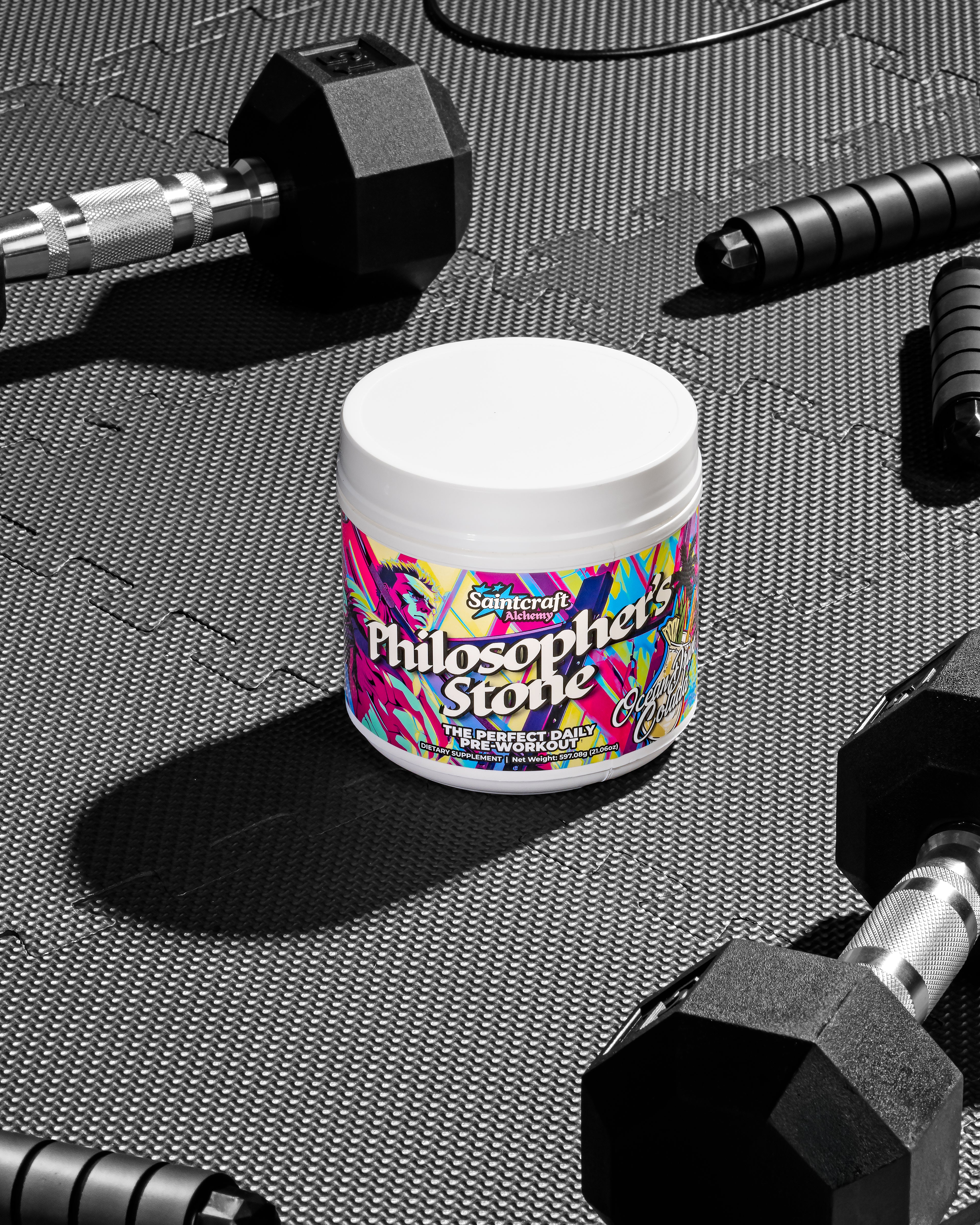 Container of 'Philosopher's Stone' supplement surrounded by dumbbells on a textured surface